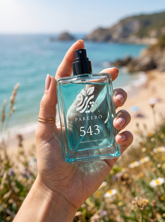 Hand holding PAREERO 543 Tommy Girl-inspired fragrance on a bright coastal day